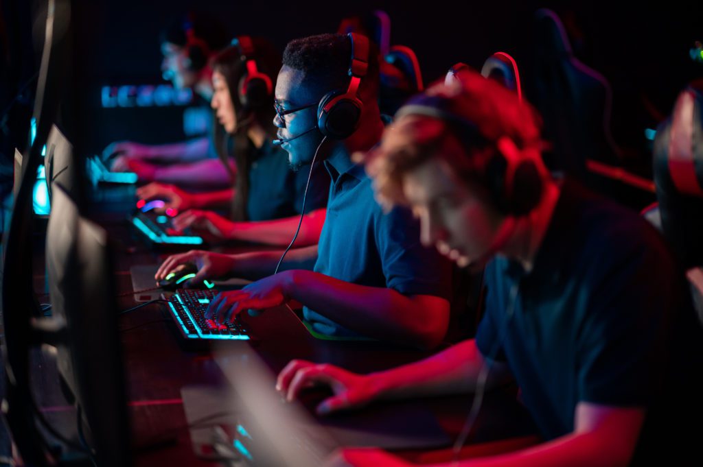 A multi-racial team of esports athletes conducts a training session before an online shooter tournament. Neon light